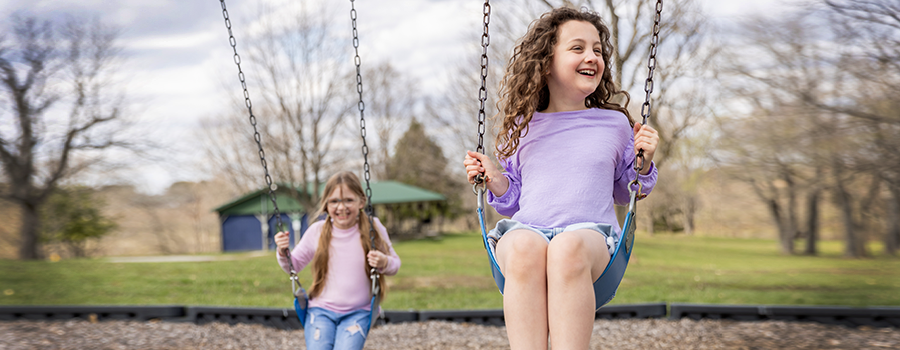 two girls swinging. One has a CGM on her leg